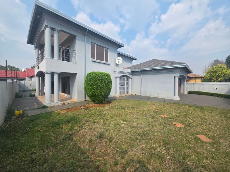 Rear view of a double-storey house featuring a balcony with metal railings, concrete columns, paved driveway, and a private garden area.