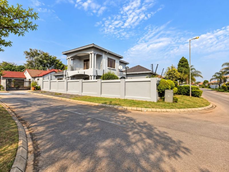 A well-maintained double-story house featuring a perimeter wall with electric fencing, a balcony with columns, and a paved driveway in a suburban setting.