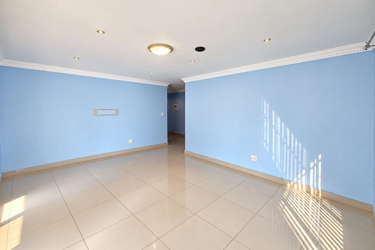 A bright, empty living area featuring light blue walls, polished porcelain floor tiles, and recessed ceiling lighting with decorative cornice detailing.