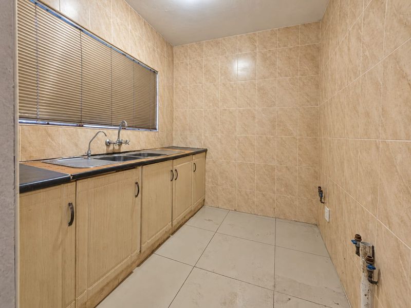 A functional laundry room featuring tiled walls, built-in cabinetry with a double basin sink, and dedicated plumbing connections for appliances.