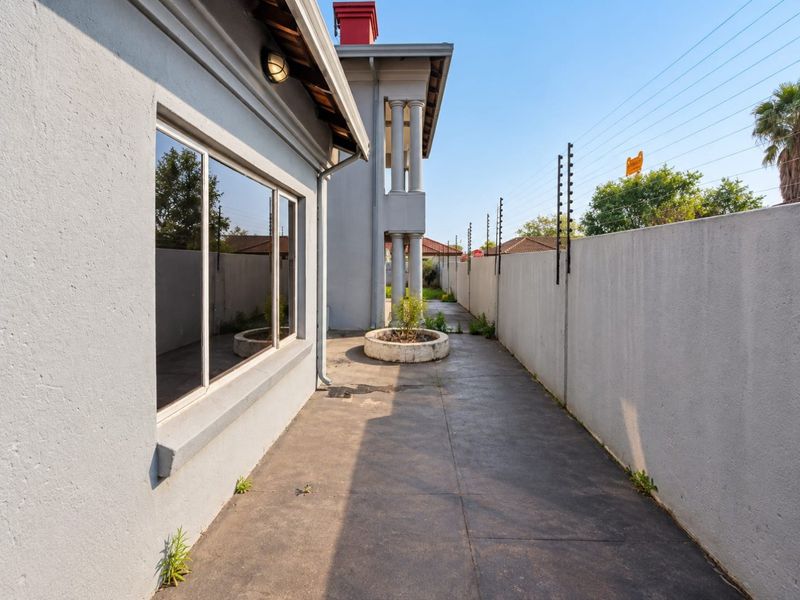 A side exterior walkway featuring concrete paving, a perimeter wall with electric fencing, and a built-in concrete planter.
