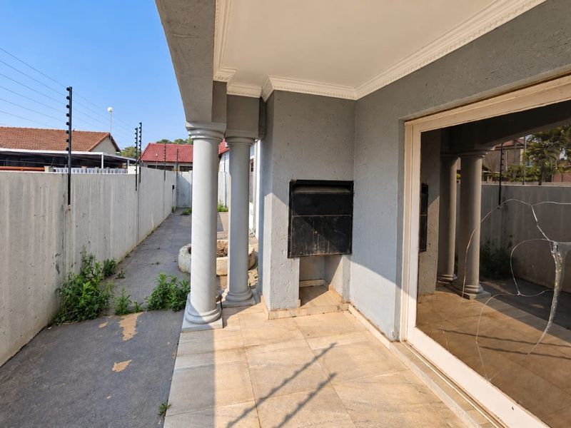 Covered patio area featuring a built-in braai, decorative columns, and tiled flooring, requiring maintenance to the sliding door and exterior finishes.
