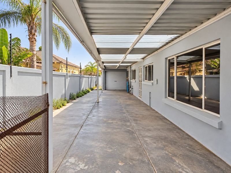 A covered outdoor driveway and walkway area featuring a corrugated metal roof, perimeter wall with electric fencing, and access to a garage.