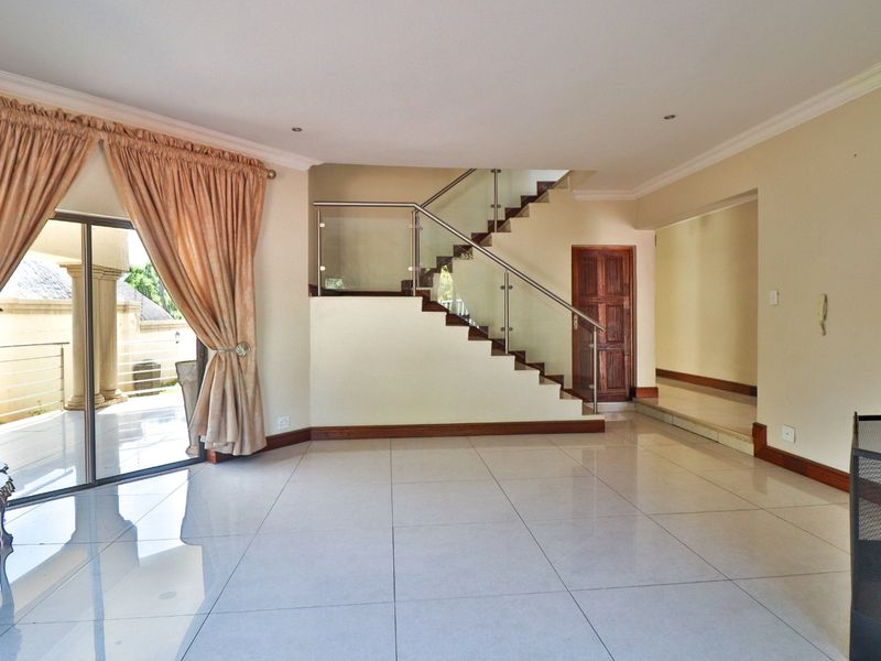Spacious living area featuring large format floor tiles, a modern staircase with glass balustrade, and direct access to an outdoor patio area.