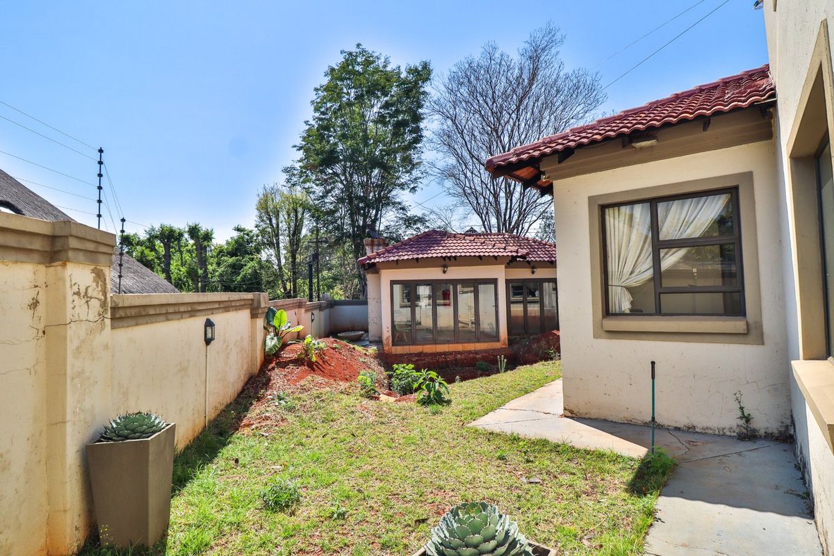 Rear garden area featuring a concrete pathway, perimeter wall with electric fencing, and views of the secondary structure with a tiled roof.