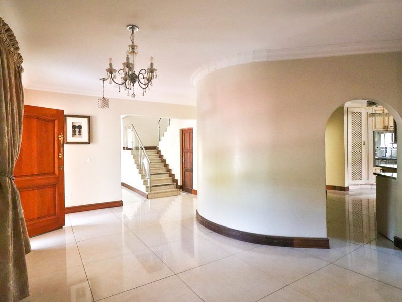 Spacious entrance hall featuring a distinctive curved wall, polished tiled flooring, and an elegant staircase with a glass balustrade leading to the upper level.