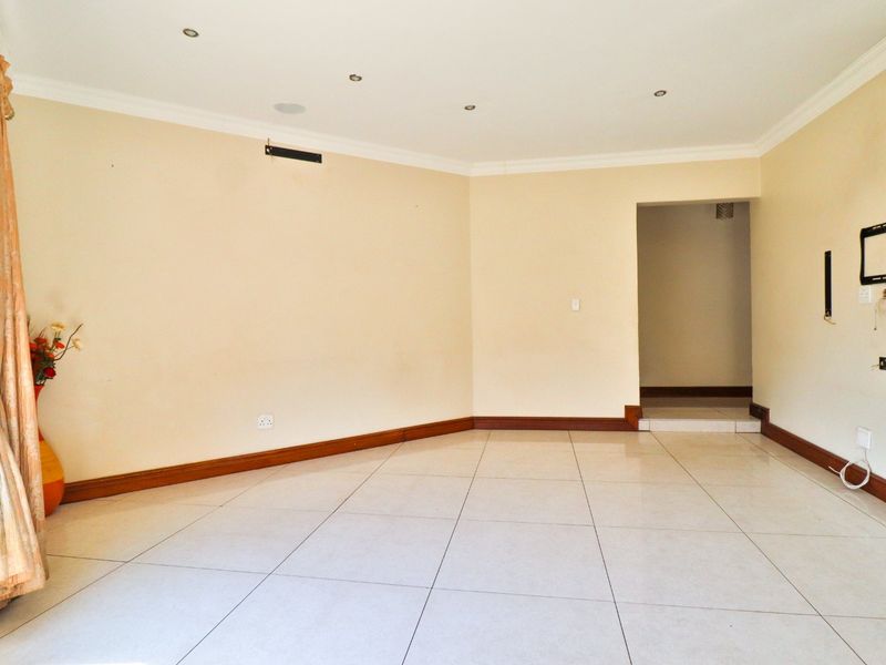 A spacious, empty living room featuring neutral tiled flooring, recessed downlighting, and coved cornicing, providing a clean canvas for interior design.