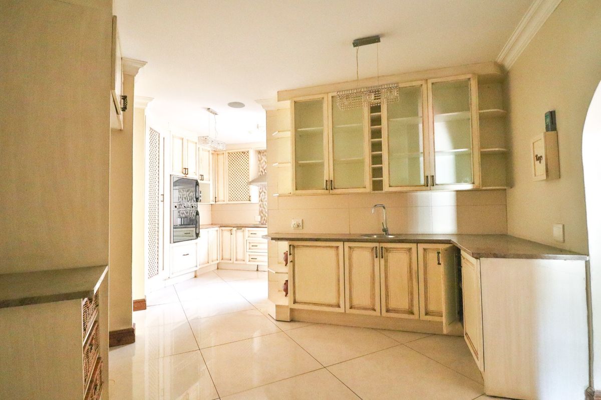 Spacious kitchen featuring cream-toned cabinetry, stone countertops, built-in oven, and glass-fronted display units with tiled flooring throughout.