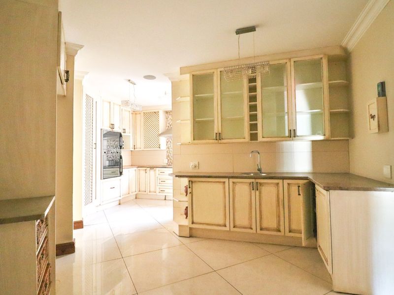 Spacious kitchen featuring cream-toned cabinetry, stone countertops, built-in oven, and glass-fronted display units with tiled flooring throughout.