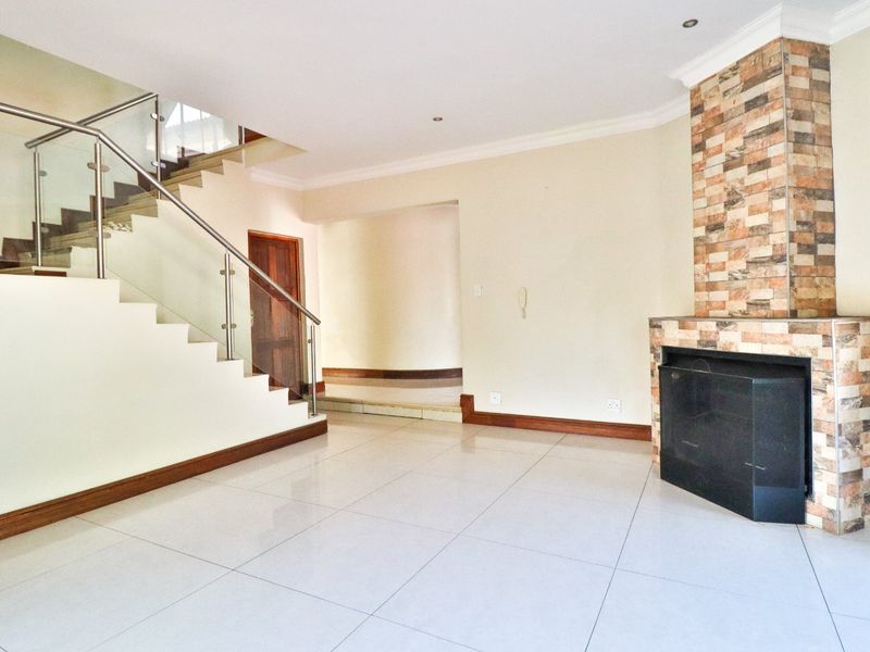 Spacious living area featuring large format floor tiles, a striking stone-clad fireplace, and a modern staircase with glass balustrades.