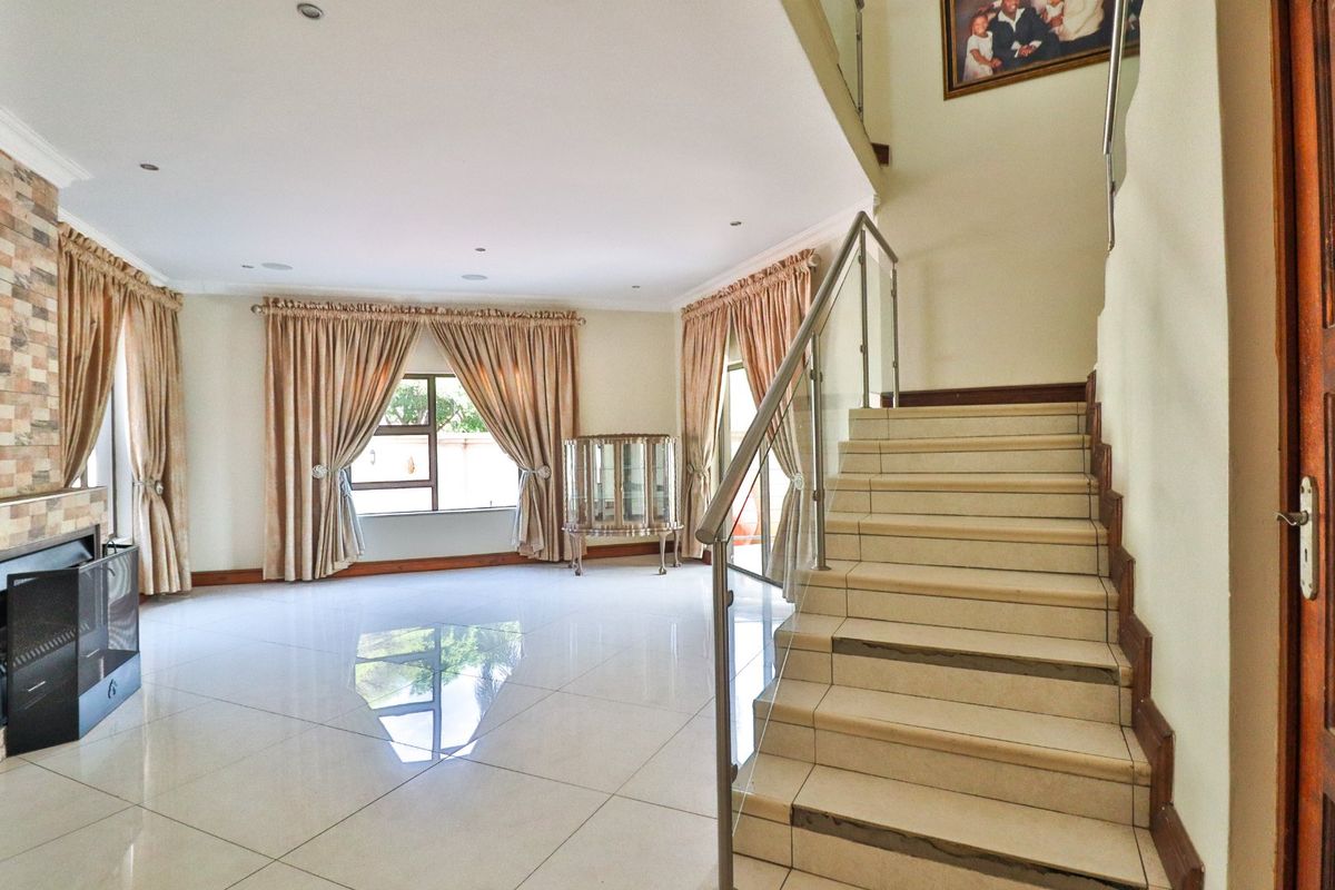 Spacious living area featuring polished tile flooring, a modern staircase with glass balustrades, and a feature fireplace with stone cladding.
