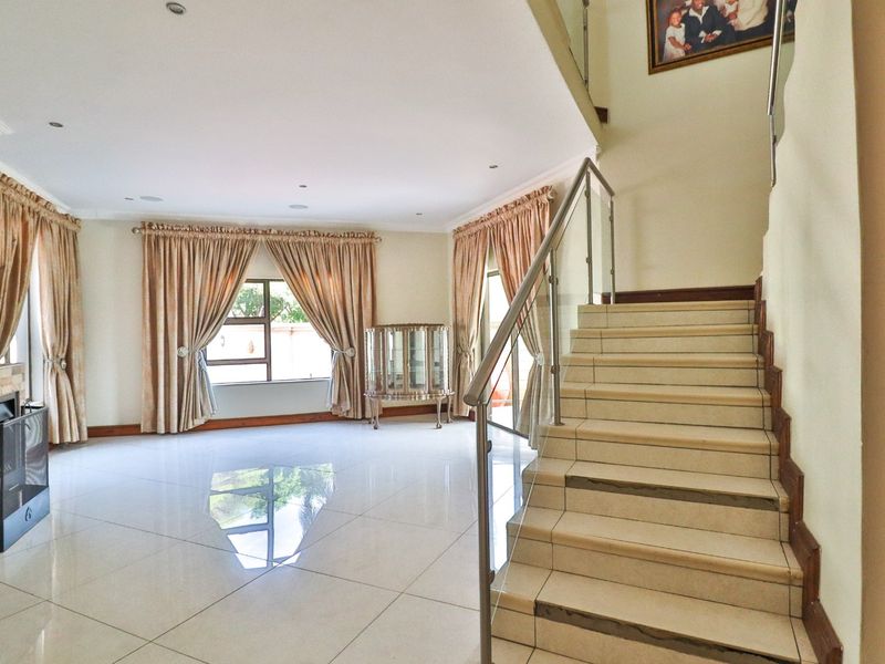 Spacious living area featuring polished tile flooring, a modern staircase with glass balustrades, and a feature fireplace with stone cladding.