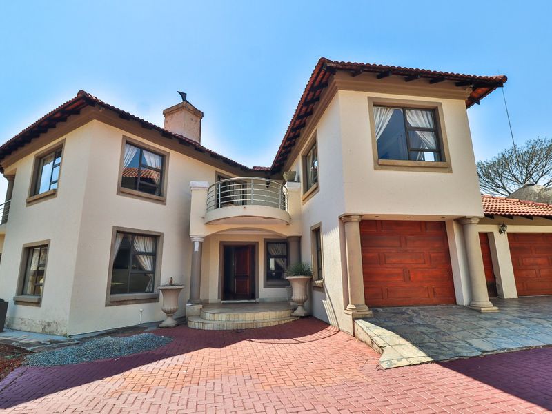Front elevation of a two-story residential house featuring a paved driveway, double garage, and a prominent balcony above the main entrance.