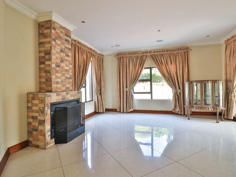 Spacious living room featuring large format floor tiles, a prominent stone-clad fireplace, and recessed lighting, offering a bright and neutral canvas.