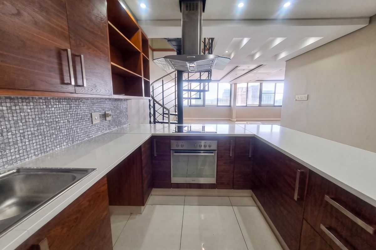 Modern kitchen featuring dark wood cabinetry, stone countertops, mosaic backsplash, and integrated stainless steel appliances, adjacent to an open-plan living area with spiral staircase.