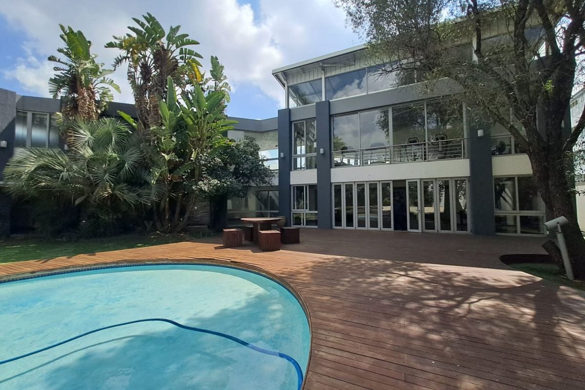 Rear exterior view of a modern apartment building featuring a swimming pool, timber decking, and expansive glass doors leading to the interior living spaces.