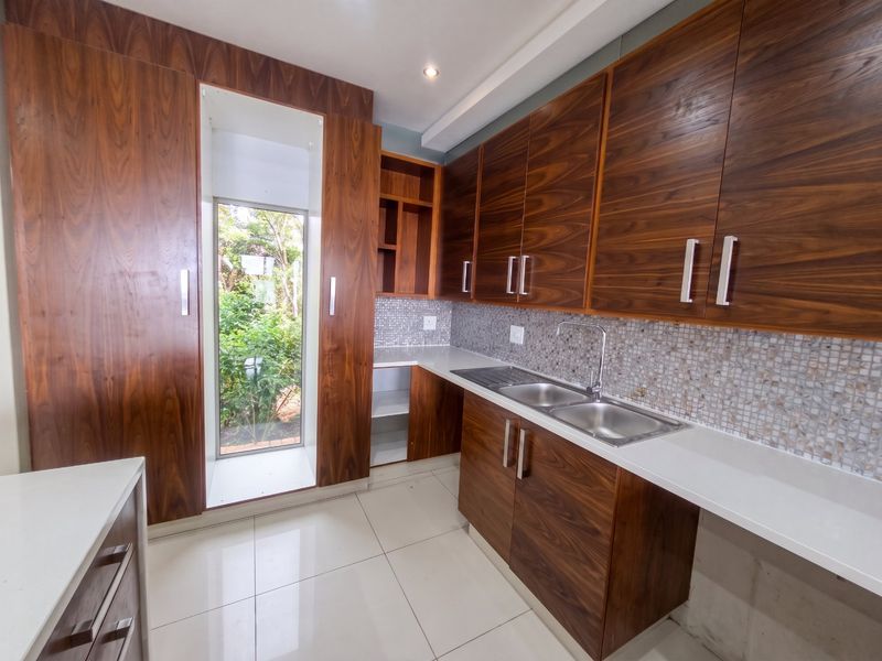 Modern kitchen featuring rich wood-grain cabinetry, stone countertops, mosaic tile backsplash, and a stainless steel double sink with a view of the garden.