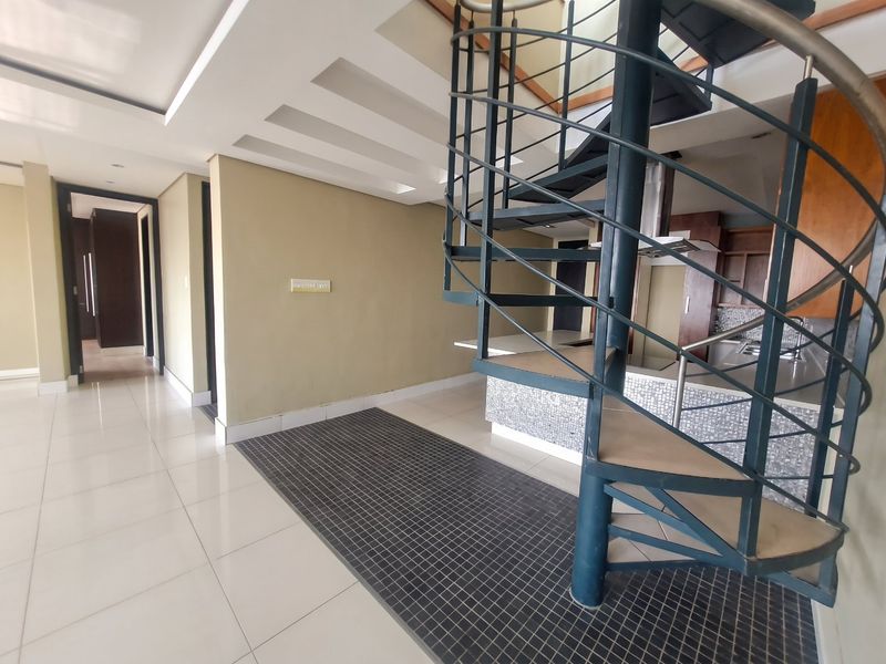 Open plan living area featuring a prominent spiral staircase, modern tiled flooring, and a kitchen area with mosaic backsplash and built-in cabinetry.