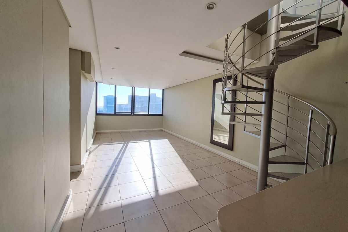 Spacious open-plan living area featuring neutral tiled flooring, recessed lighting, and a modern metal spiral staircase leading to the upper level.