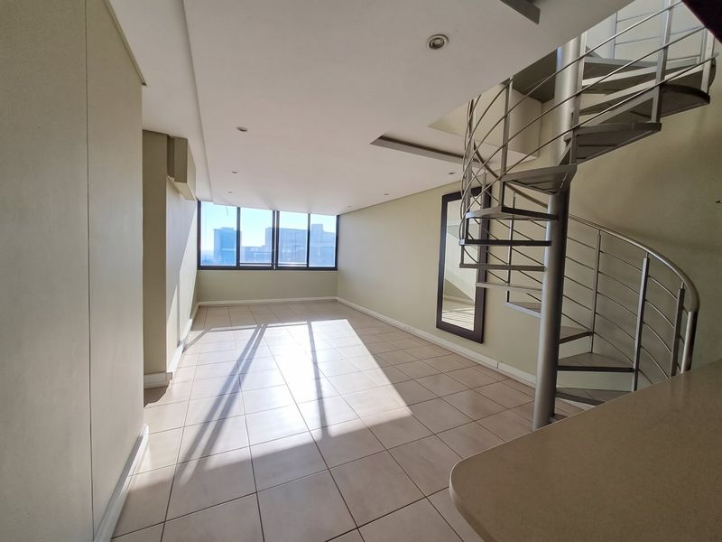 Spacious open-plan living area featuring neutral tiled flooring, recessed lighting, and a modern metal spiral staircase leading to the upper level.