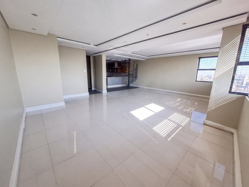 Spacious open-plan living area featuring polished porcelain tiles, recessed ceiling lighting, and a unique spiral staircase leading to an upper level.