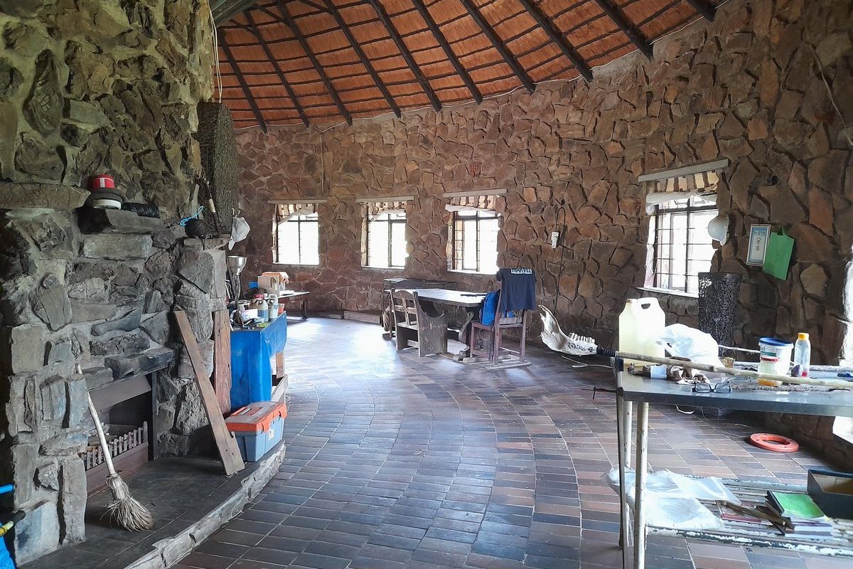 Spacious living area featuring rustic stone walls, a large stone fireplace, and a traditional thatched roof with tiled flooring.