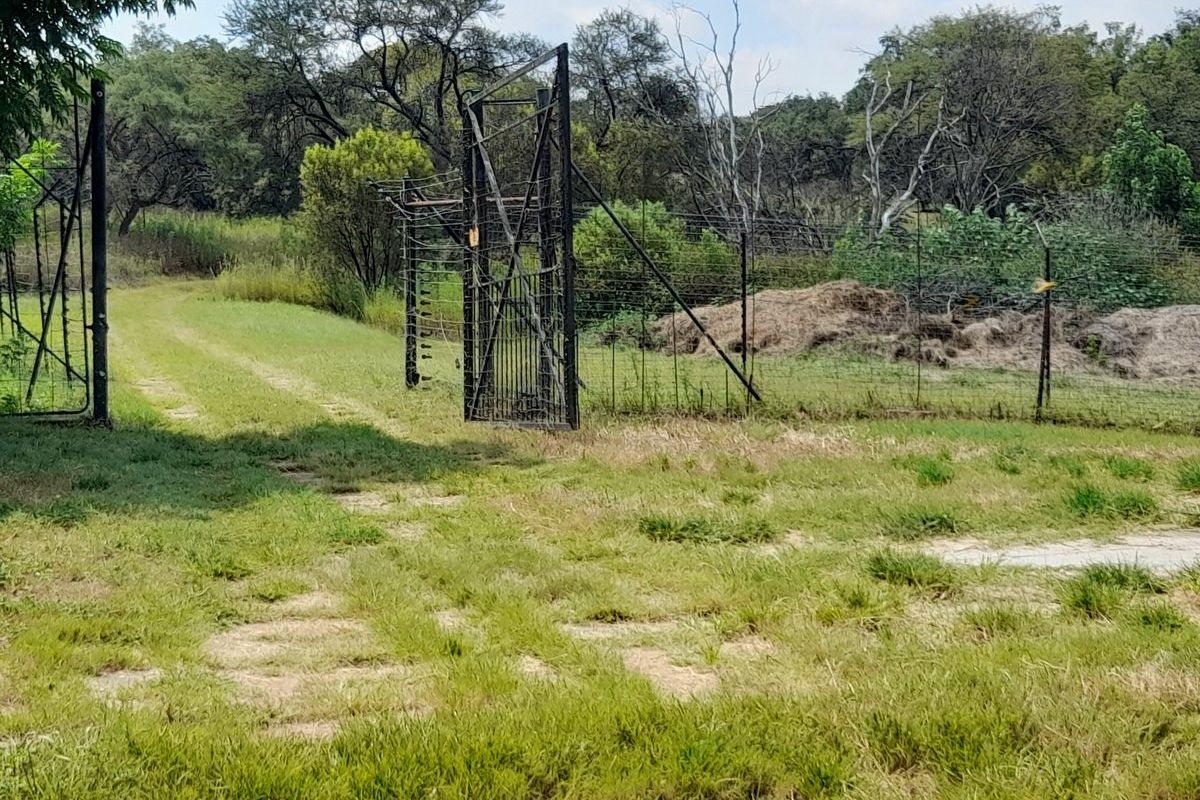 A rural farm entrance featuring a metal gate and wire fencing with visible signs of wear and weathering.