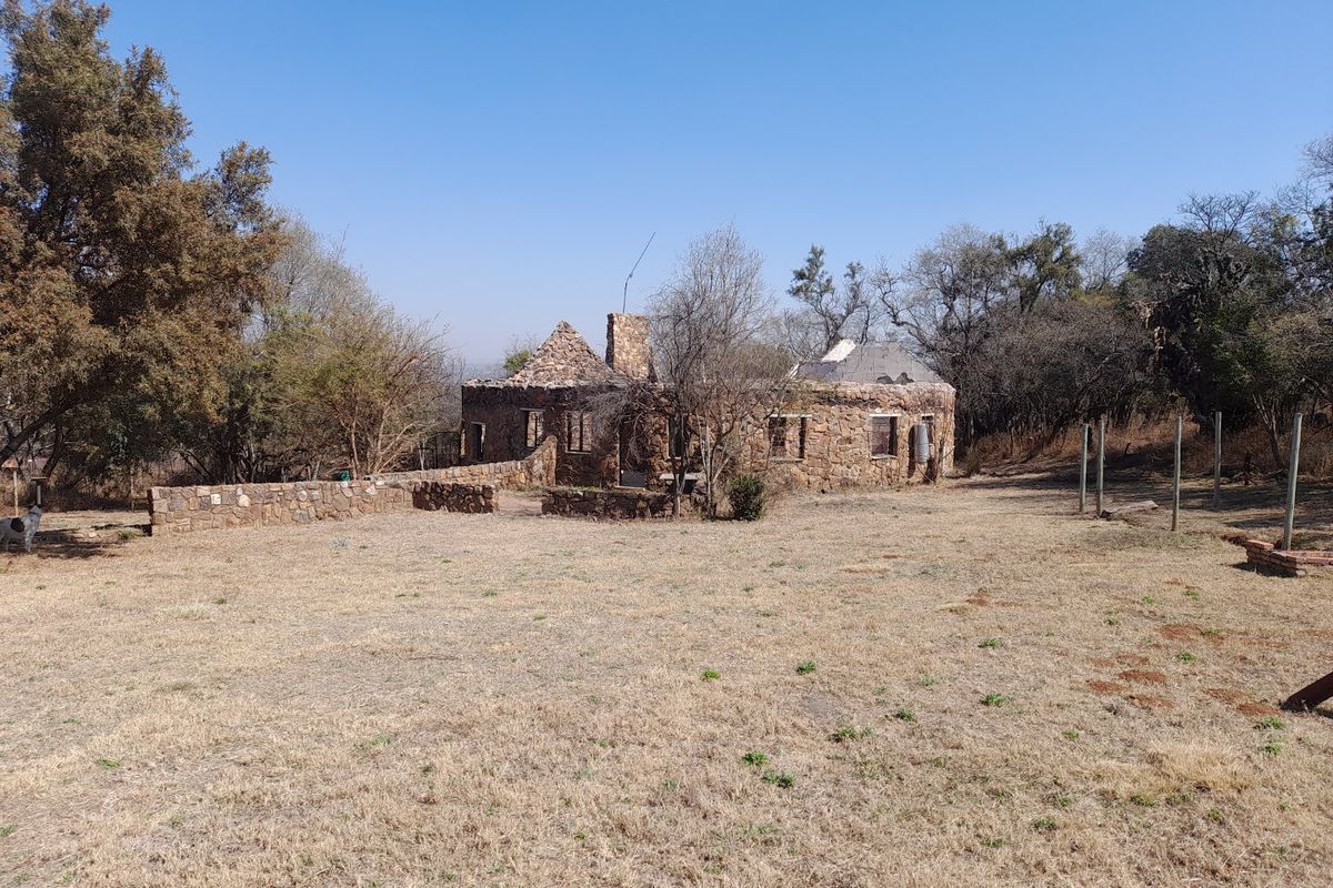 A dilapidated stone farmhouse structure showing significant structural deterioration and missing roof sections, situated on a large rural plot.