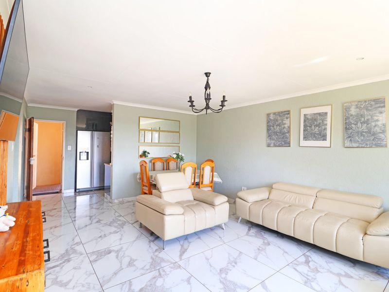 Spacious open-plan living and dining area featuring polished marble-look floor tiles, neutral wall tones, and integrated kitchen cabinetry.