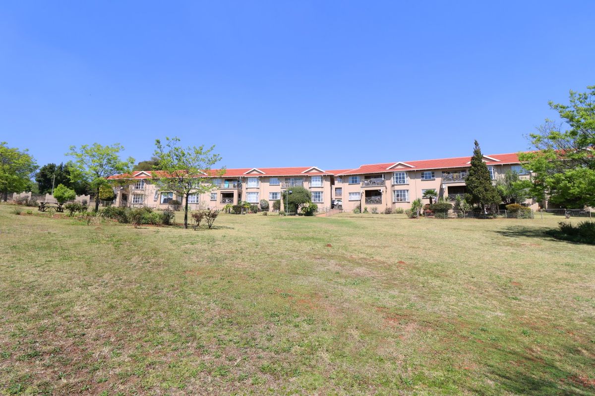 A wide-angle view of the apartment complex exterior, featuring a large communal lawn area and multi-story residential units with balconies.