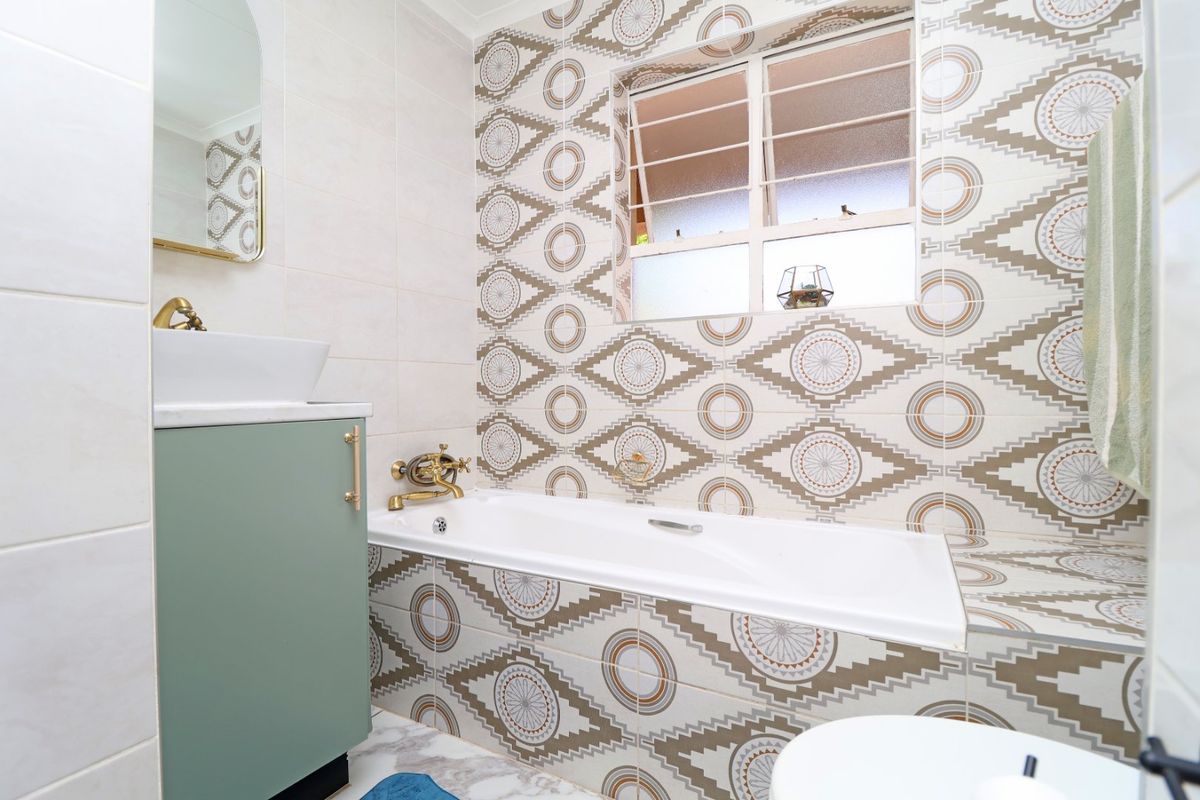 A well-maintained bathroom featuring a built-in bathtub, a modern vanity with a vessel sink, and distinctive patterned wall tiling.