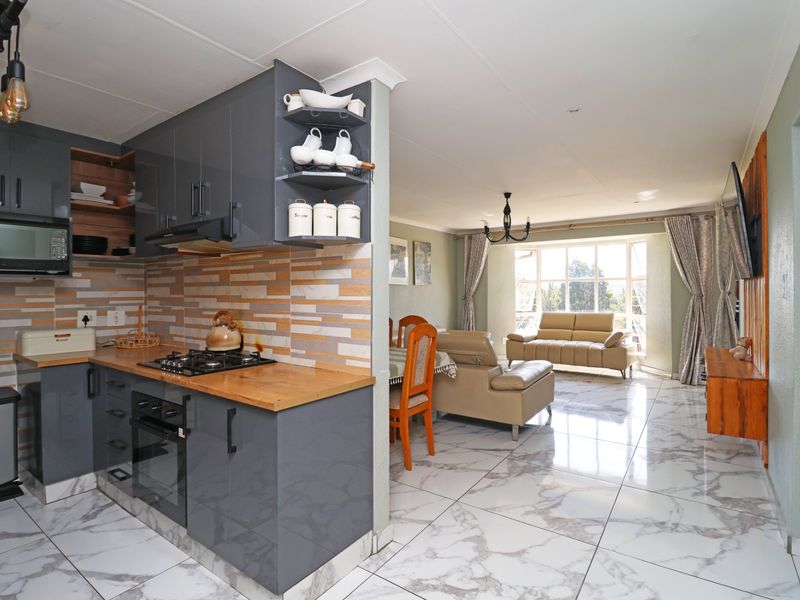 Modern open-plan living area featuring a contemporary kitchen with grey cabinetry, gas hob, and marble-look tiled flooring throughout the combined space.