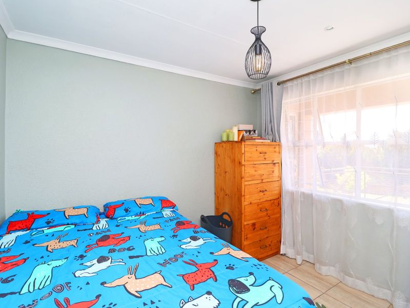 A well-lit bedroom featuring tiled flooring, neutral wall finishes, and a modern pendant light fixture, offering a comfortable and functional living space.