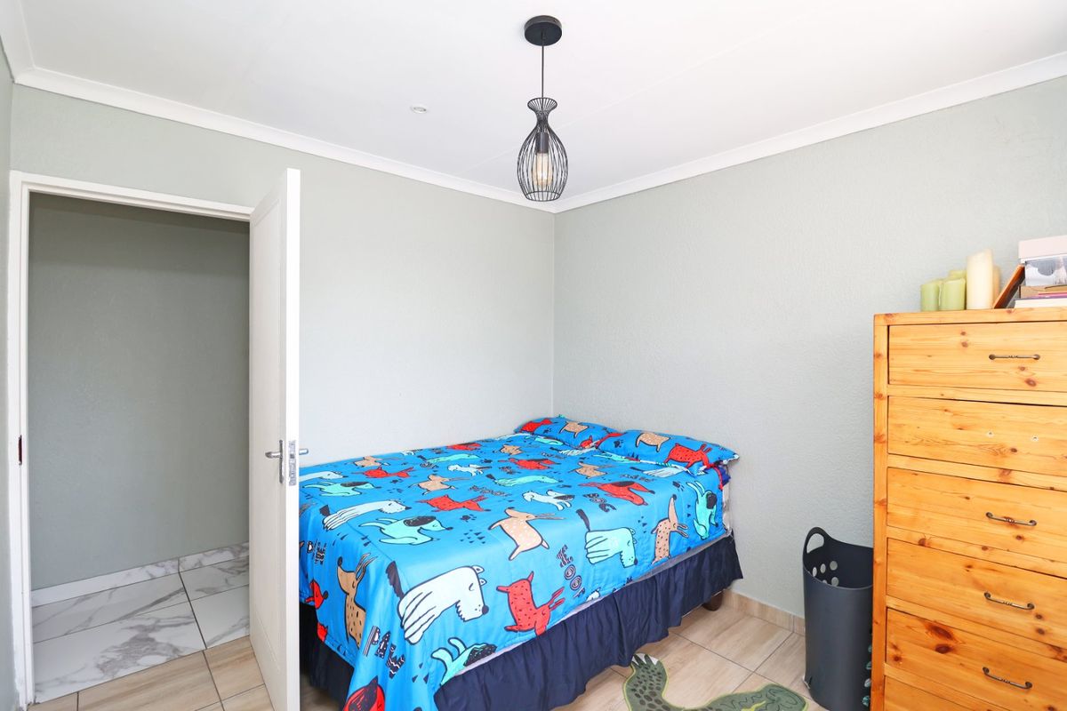 A functional bedroom featuring tiled flooring, coved ceilings, and a modern pendant light fixture, providing a clean and neutral space.
