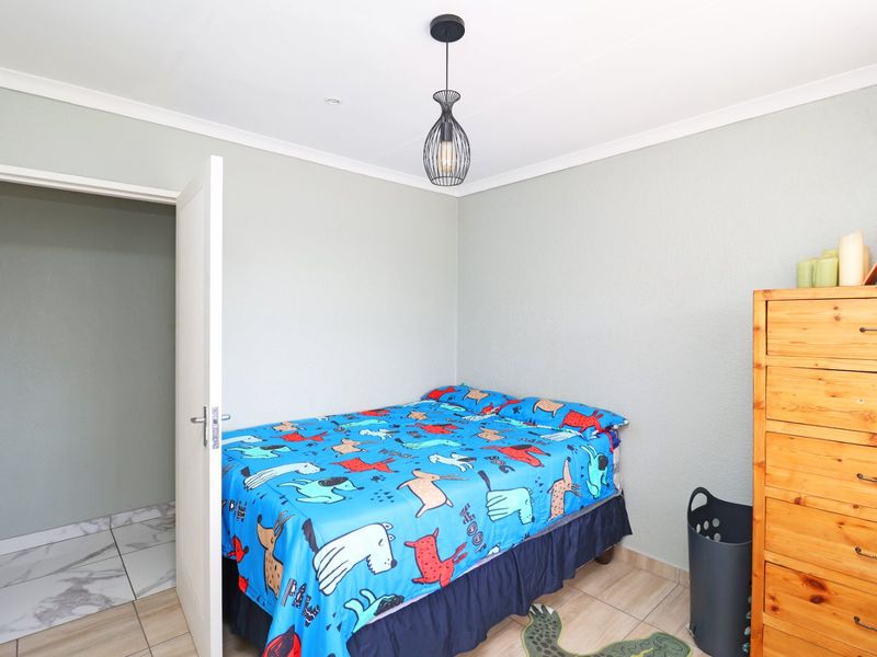 A functional bedroom featuring tiled flooring, coved ceilings, and a modern pendant light fixture, providing a clean and neutral space.