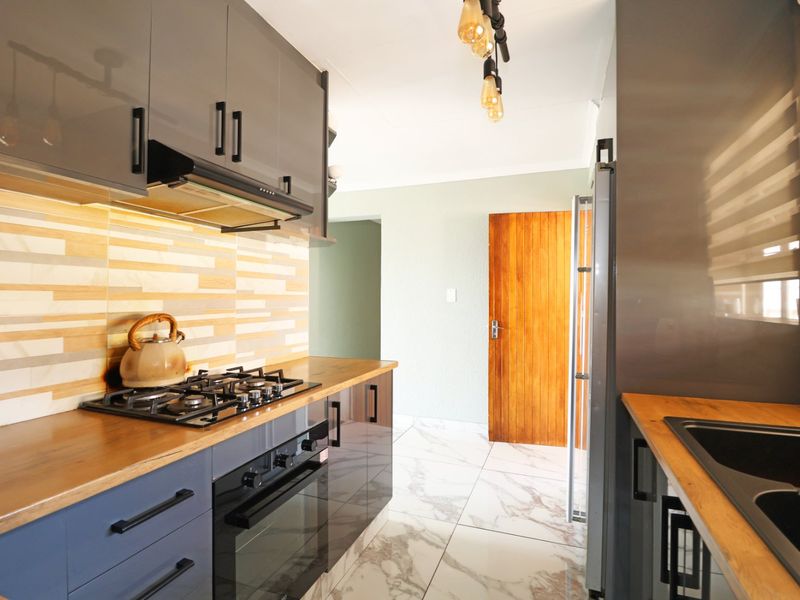 Modern kitchen featuring high-gloss cabinetry, gas hob, built-in oven, extractor fan, and stylish marble-look tiled flooring with warm under-cabinet lighting.