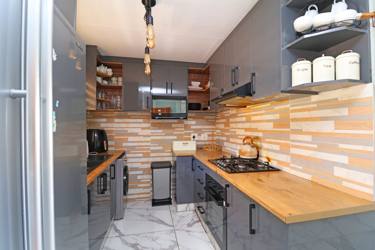 Modern galley kitchen featuring grey high-gloss cabinetry, wooden countertops, gas hob, built-in oven, and stylish stone-look tile backsplash.