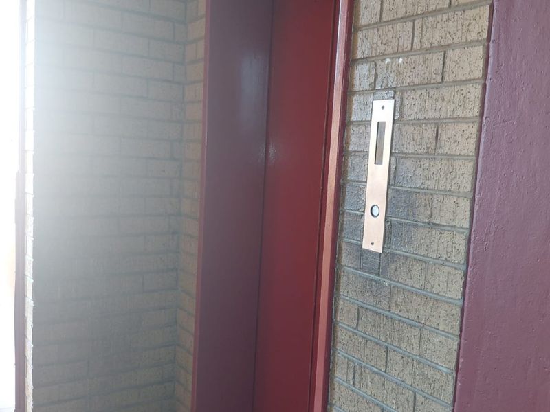 A communal hallway area featuring a red elevator door set against a brick wall with tiled flooring.