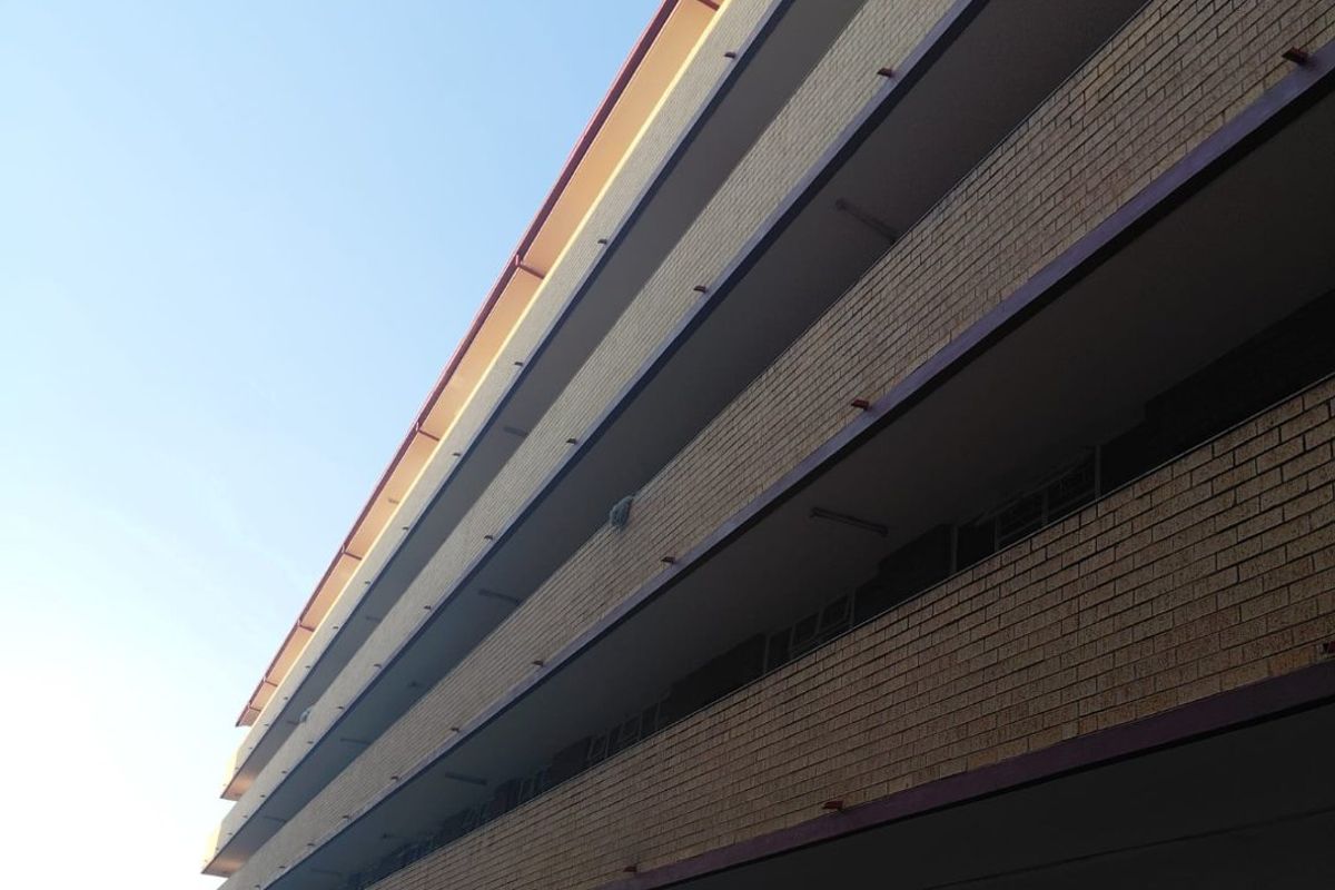 A low-angle exterior view of a multi-story apartment building featuring a brick facade and open-air balcony walkways.