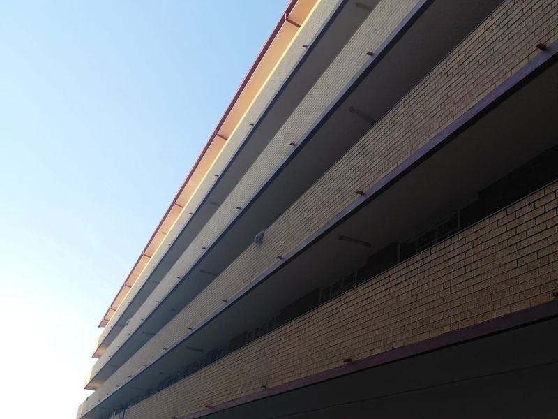 A low-angle exterior view of a multi-story apartment building featuring a brick facade and open-air balcony walkways.