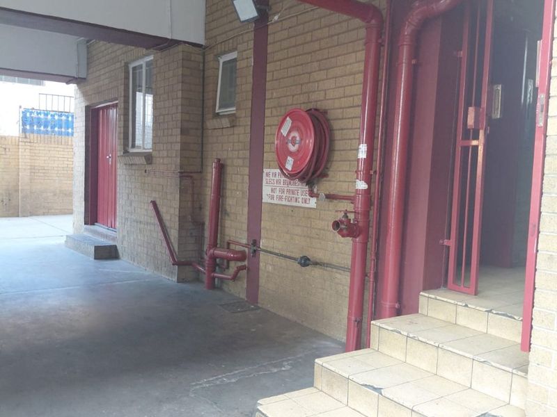Exterior entrance area of an apartment building featuring brick facade, tiled steps, and essential fire safety equipment including a hose reel and hydrant.