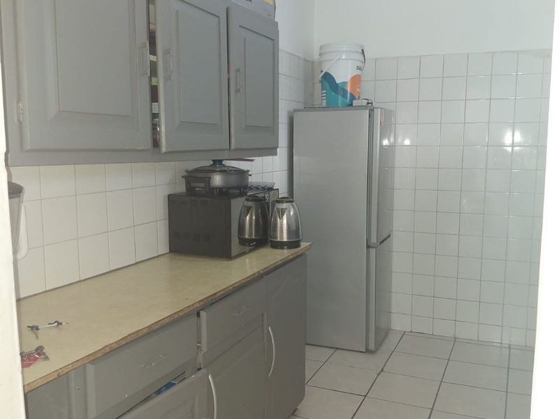 A functional kitchen featuring grey built-in cabinetry, laminate countertops, and white ceramic wall and floor tiling.