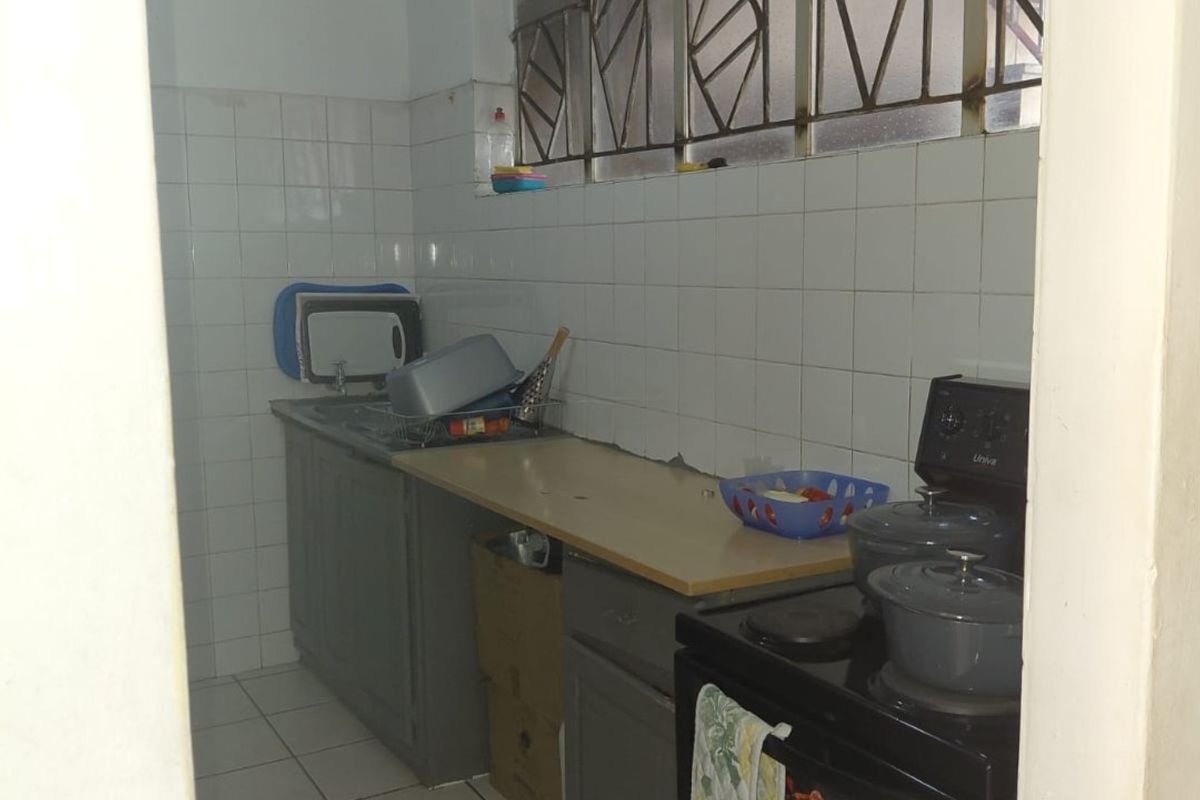 A compact kitchen featuring tiled flooring, a tiled splashback, built-in cabinetry, and a freestanding stove, with security bars installed on the windows.