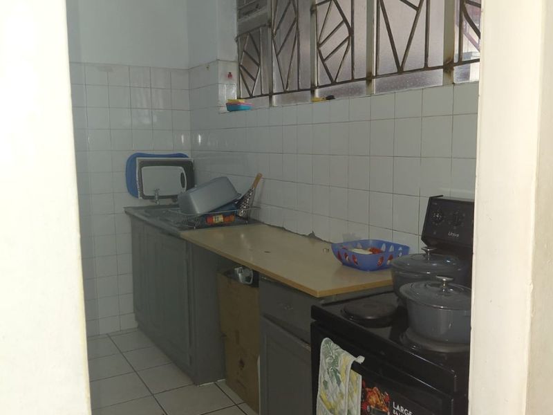 A compact kitchen featuring tiled flooring, a tiled splashback, built-in cabinetry, and a freestanding stove, with security bars installed on the windows.