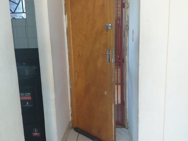 Entryway featuring tiled flooring, a wooden door, and an external security gate, showing signs of wear and requiring maintenance.