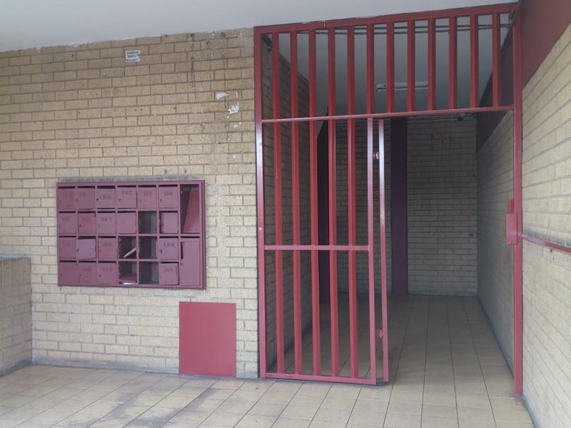Apartment building entrance lobby featuring brick walls, tiled flooring, and a metal security gate with integrated mailboxes.