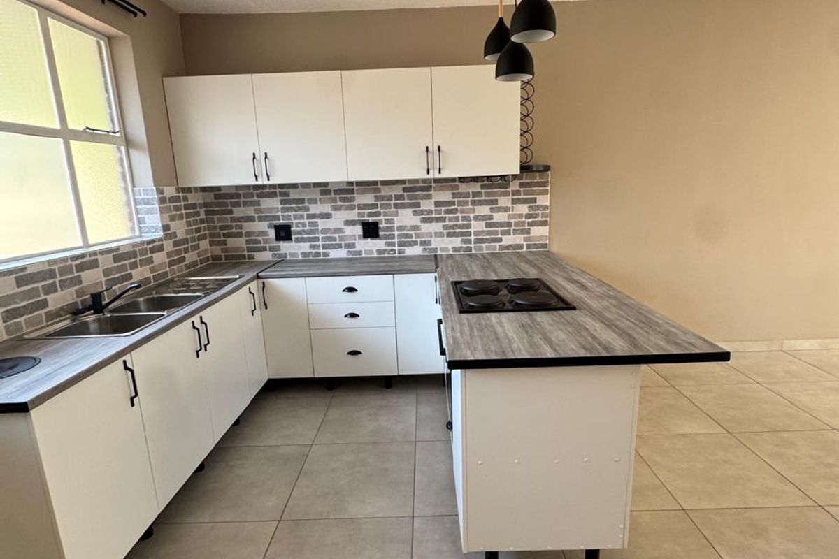 Modern kitchen featuring white cabinetry, wood-look laminate countertops, an integrated electric hob, double sink, and stylish brick-patterned backsplash with neutral floor tiles.