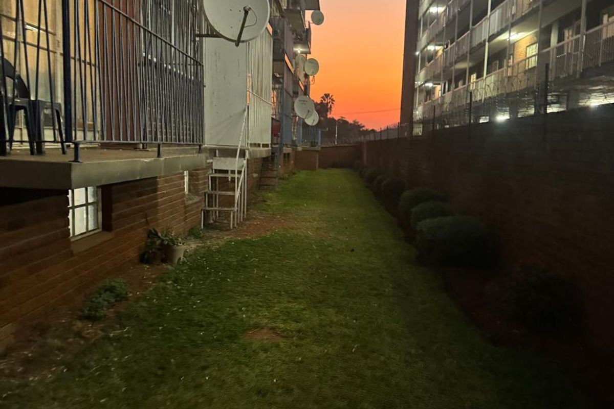 A view of the rear exterior area of the apartment building, featuring a lawn, brick boundary wall, and multiple satellite dishes mounted on the facade.