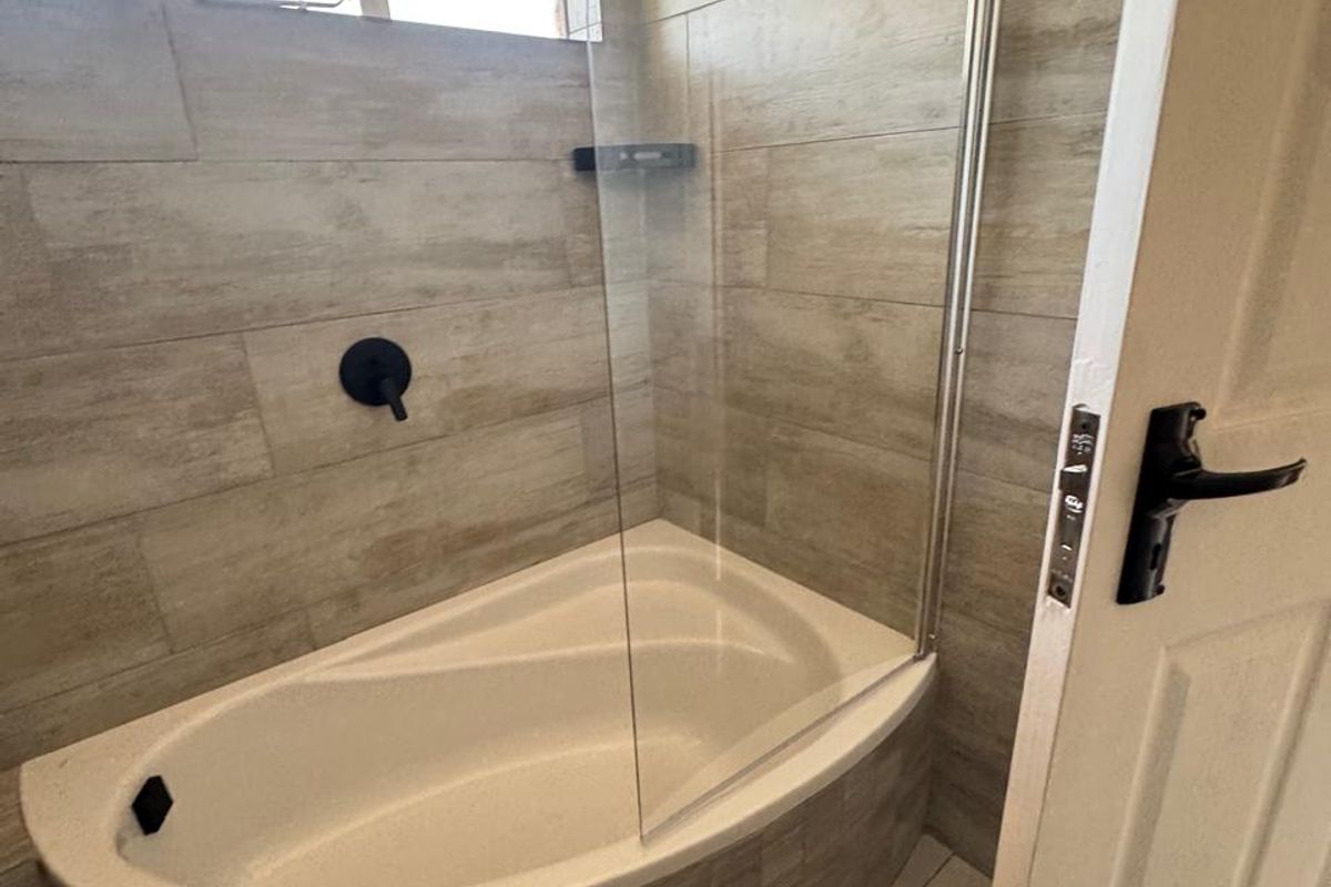 Modern bathroom featuring a built-in bathtub with a glass shower screen, rain shower head, and contemporary wood-look wall tiling.