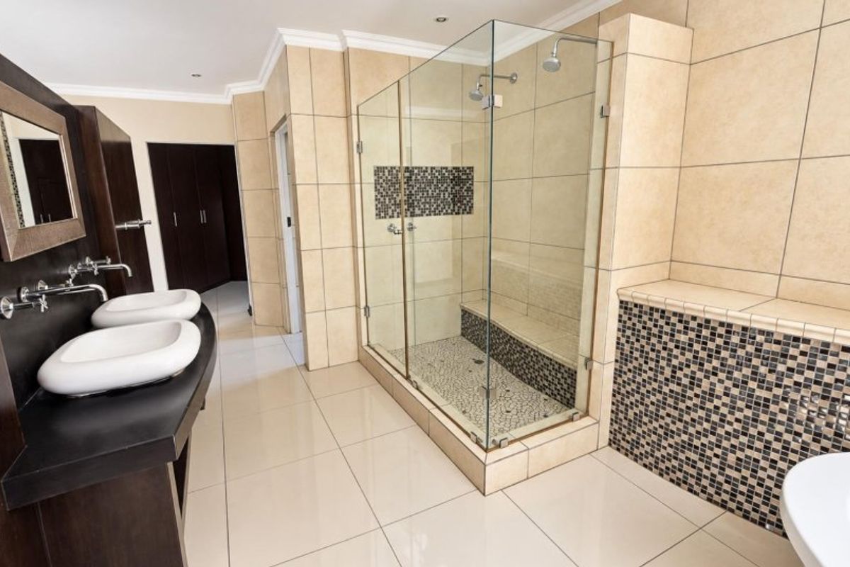 Modern bathroom featuring a double vanity with wall-mounted faucets, a spacious glass-enclosed shower with a built-in bench, and elegant mosaic tile detailing.